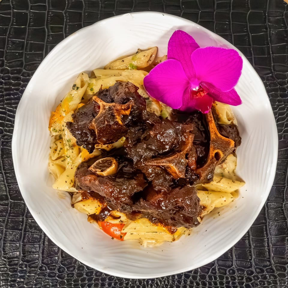 Mr Mack's oxtail pasta dish, garnished with a vibrant purple orchid, on a white plate.