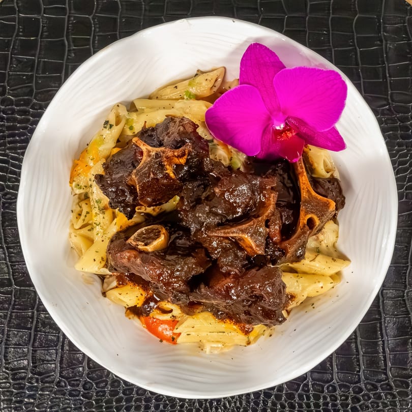 Mr Mack's oxtail pasta dish, garnished with a vibrant purple orchid, on a white plate.