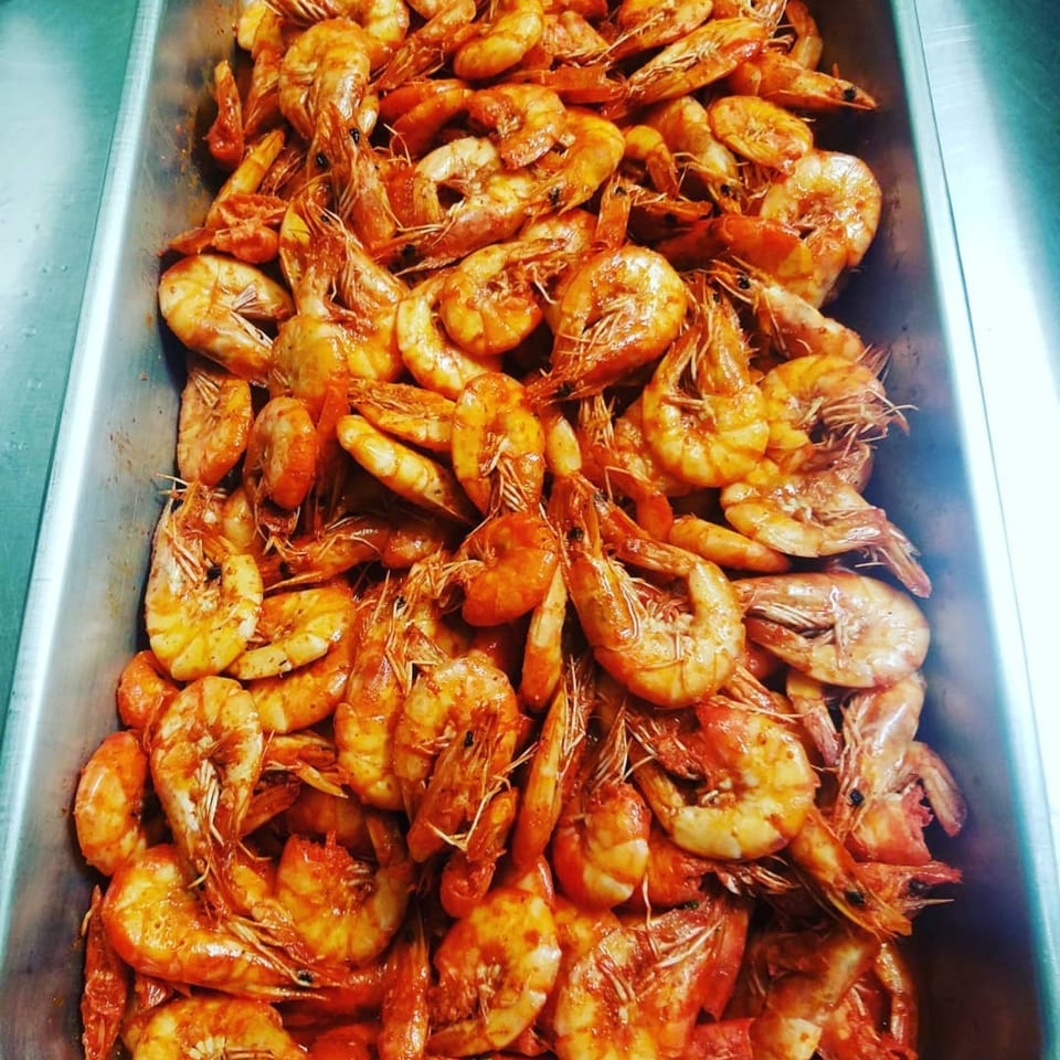 A metal tray overflowing with cooked, seasoned Jamaican-style shrimp, ready to be served.