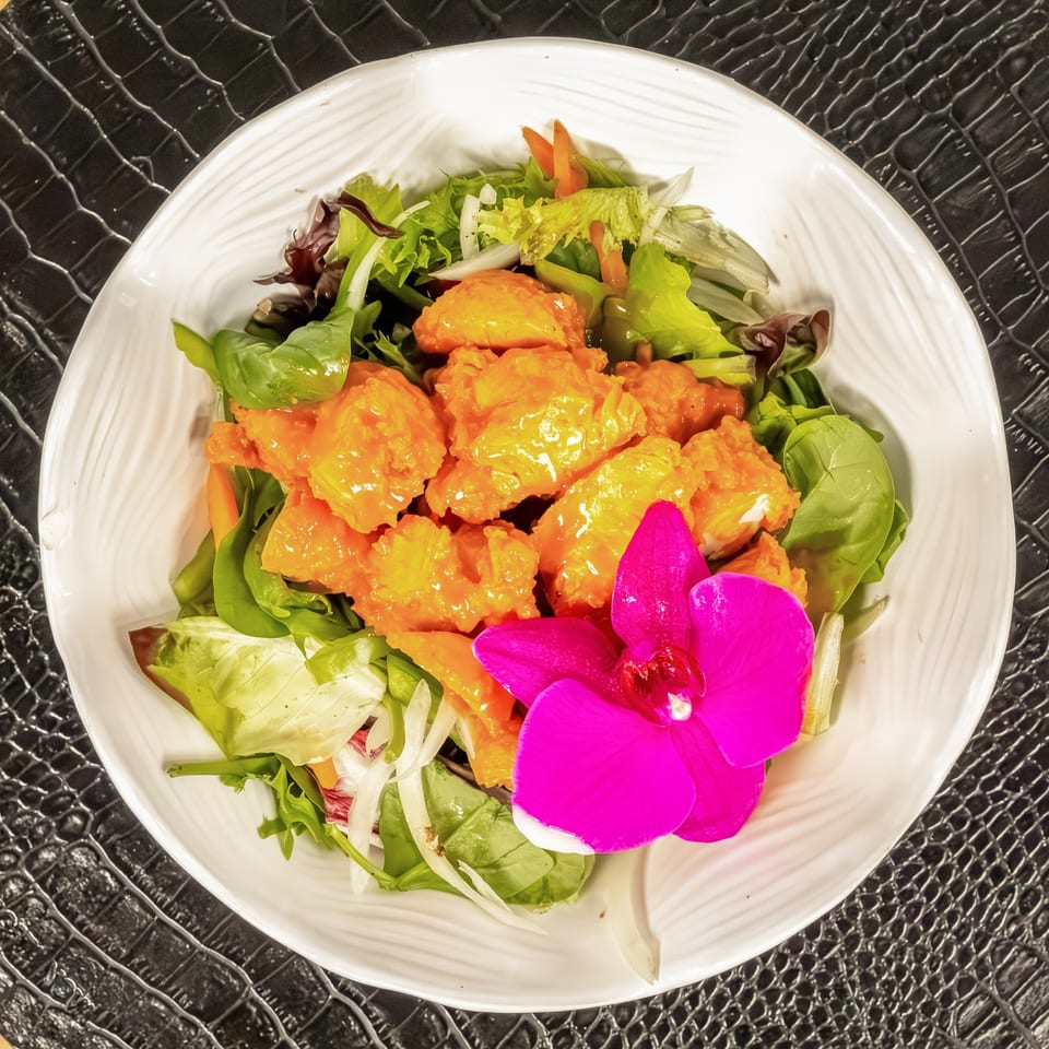 Mr Mack's jerk chicken salad with mixed greens, carrots, onions, and a pink orchid garnish.
