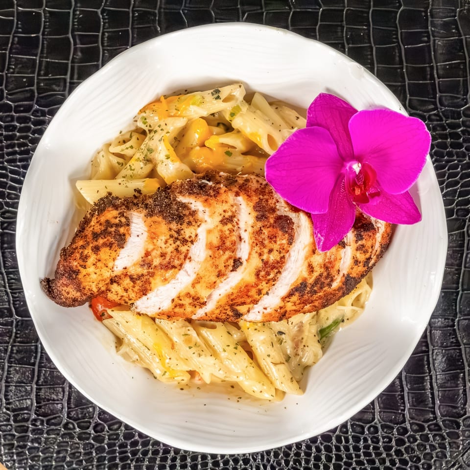 Mr Mack's jerk chicken pasta with penne, creamy sauce, and a pink orchid garnish.