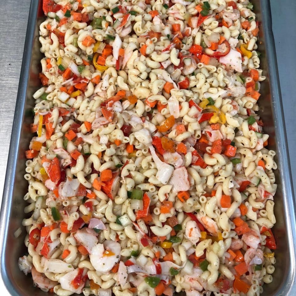 A large tray of Mr Mack's Jamaican macaroni salad with shrimp, crab, and colorful vegetables.