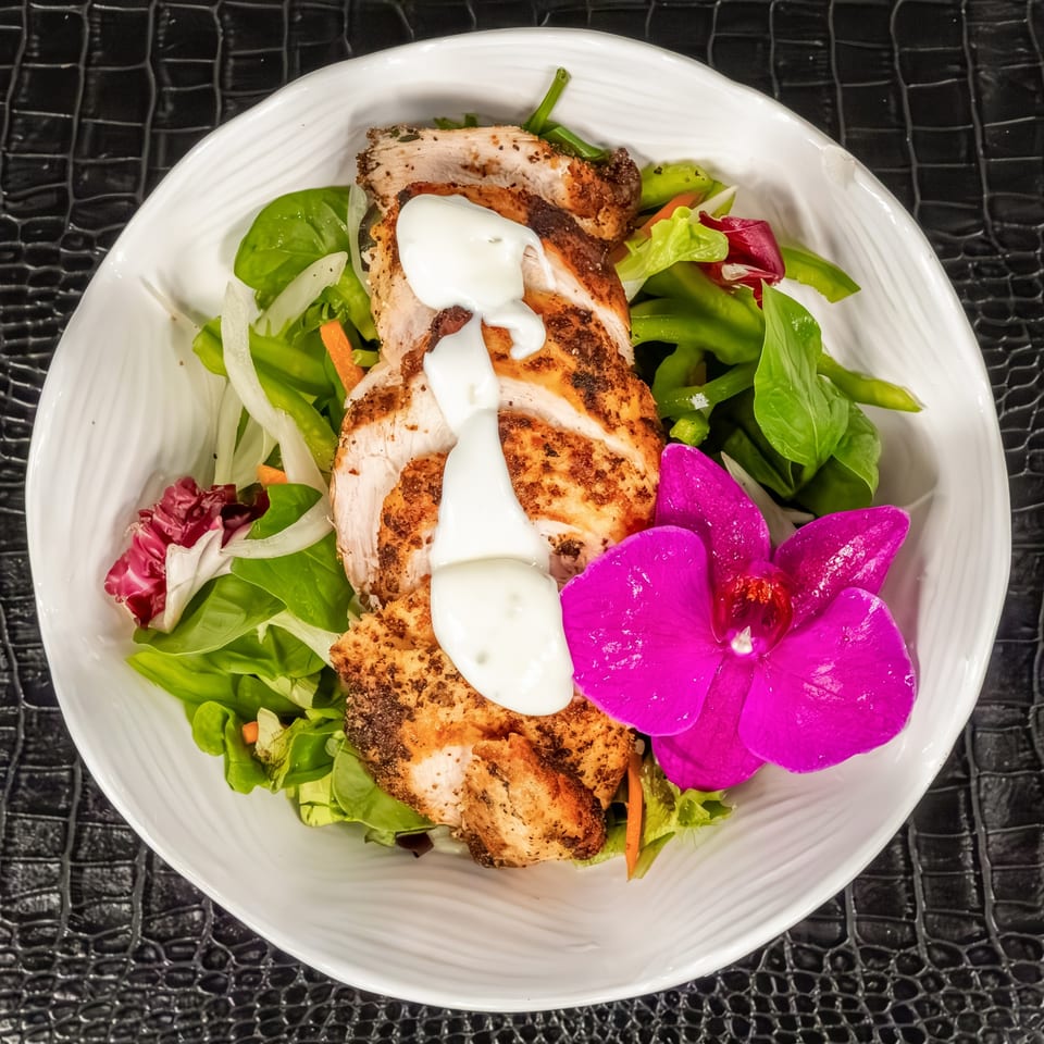 Mr Mack's jerk chicken salad with greens, onions, carrots, and a vibrant pink orchid.